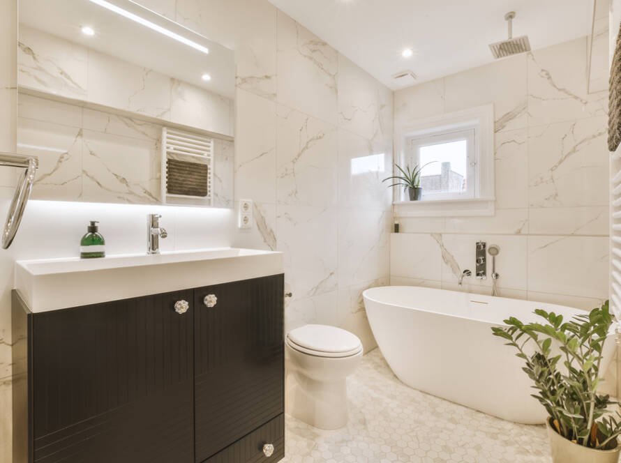 Salle de bain élégante avec baignoire, murs en marbre et meuble vasque moderne.